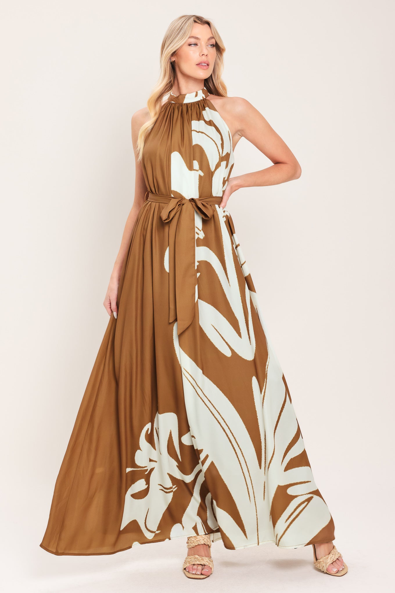 Woman wearing a brown maxi dress featuring halter neckline with back neck button closure, sleeveless and self sash tie | Flying Tomato