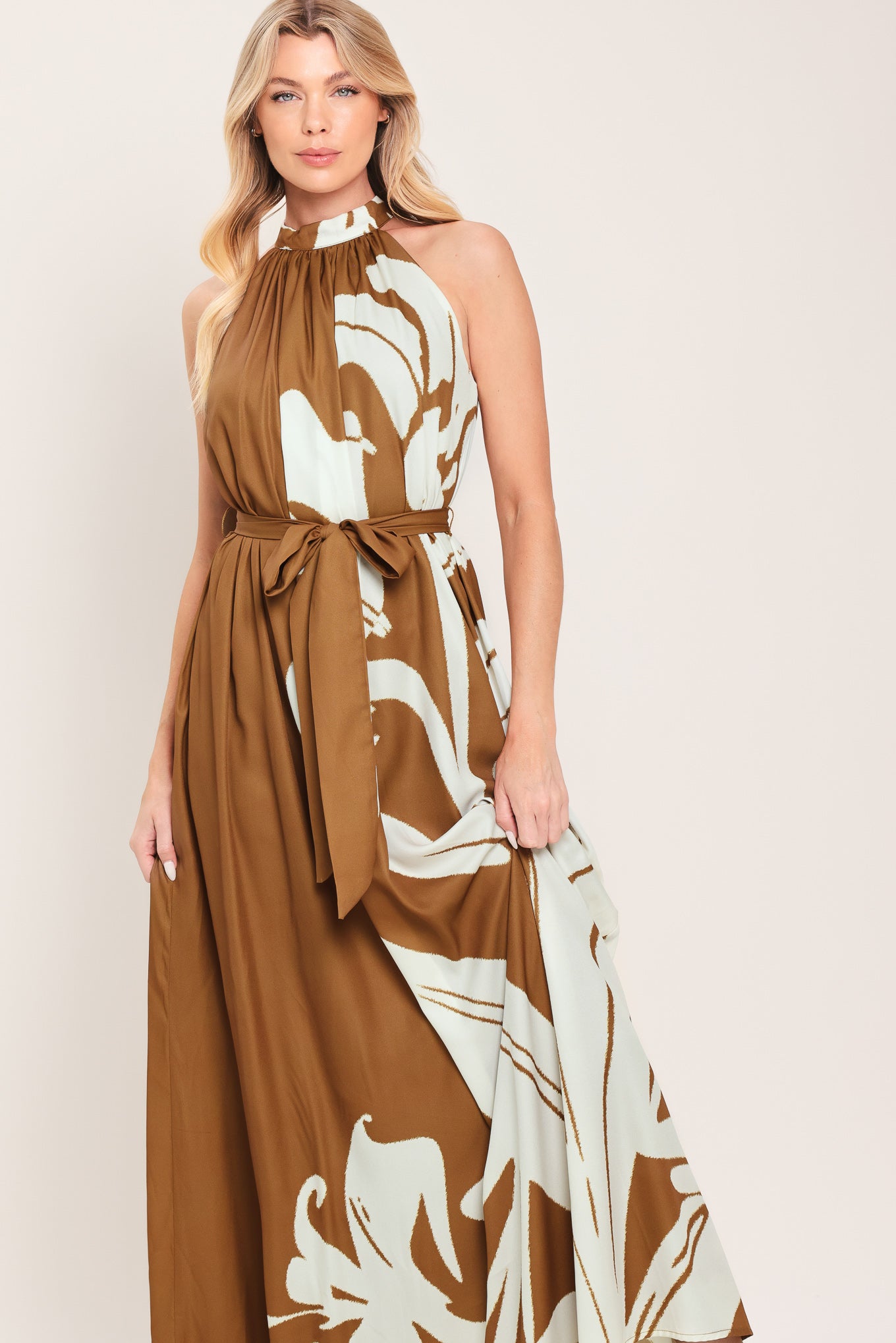 Woman wearing a brown maxi dress featuring halter neckline with back neck button closure, sleeveless and self sash tie | Flying Tomato