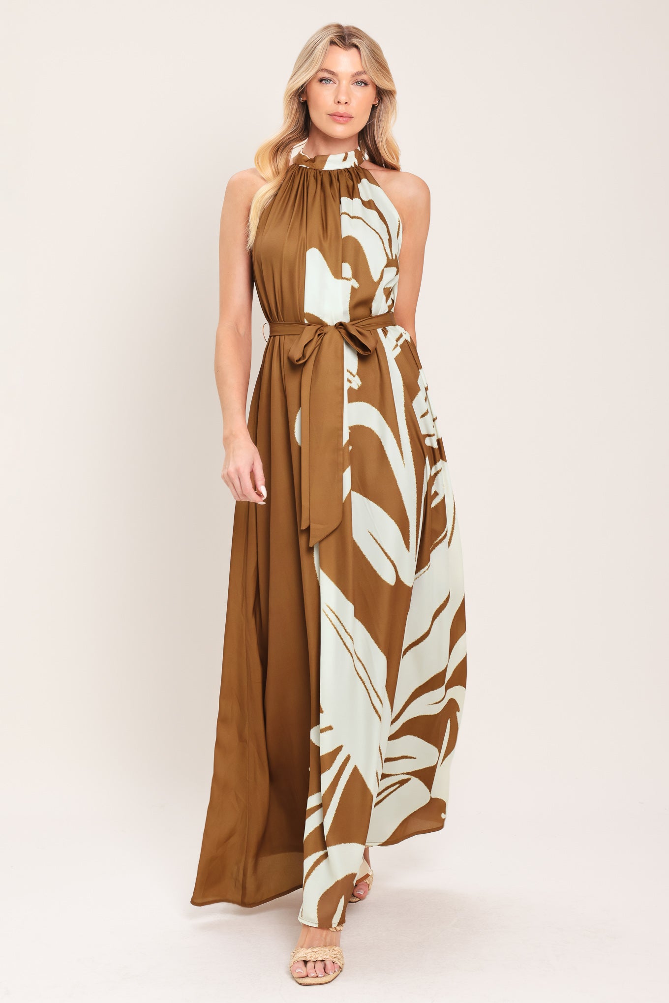 Woman wearing a brown maxi dress featuring halter neckline with back neck button closure, sleeveless and self sash tie | Flying Tomato