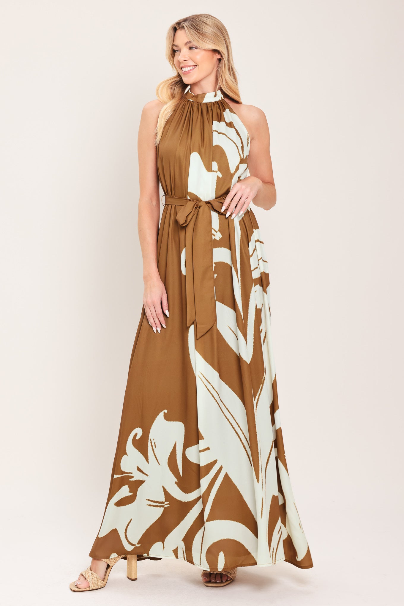 Woman wearing a brown maxi dress featuring halter neckline with back neck button closure, sleeveless and self sash tie | Flying Tomato