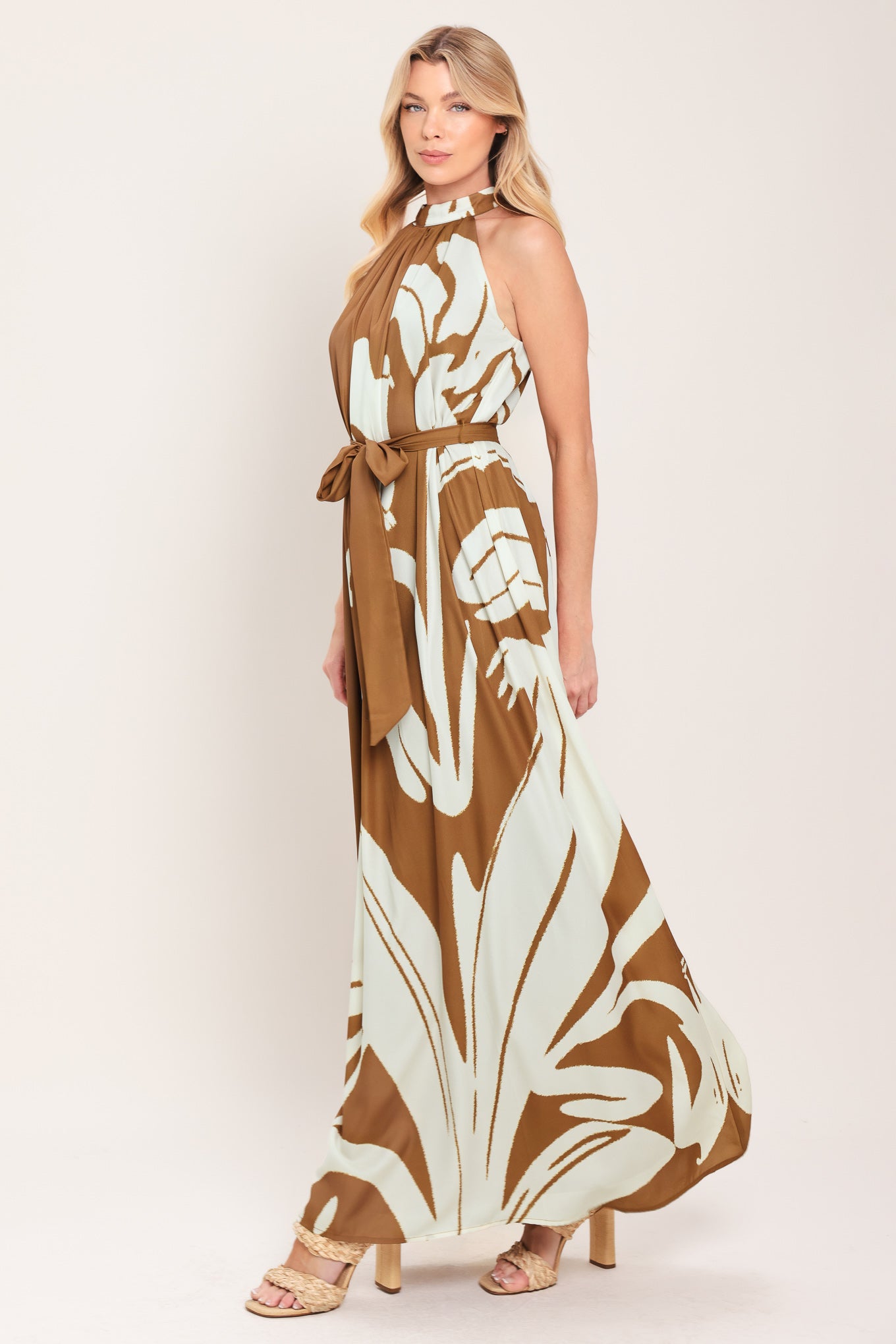 Woman wearing a brown maxi dress featuring halter neckline with back neck button closure, sleeveless and self sash tie | Flying Tomato