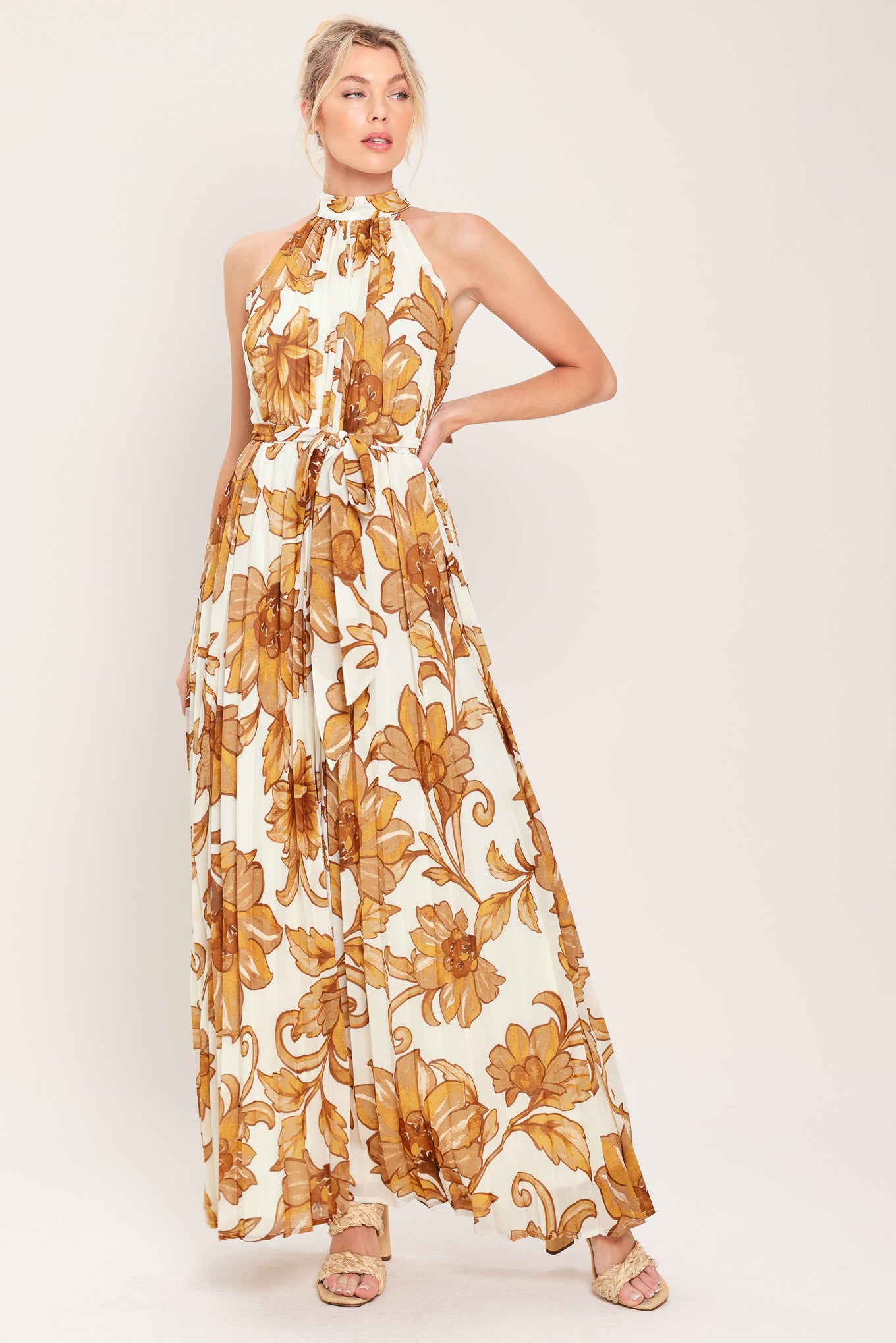 Woman wearing an ivory with brown floral print maxi dress with halter neckline with tie back, pleated body and self sash tie | Flying Tomato