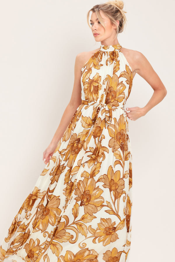 Woman wearing an ivory with brown floral print maxi dress with halter neckline with tie back, pleated body and self sash tie | Flying Tomato