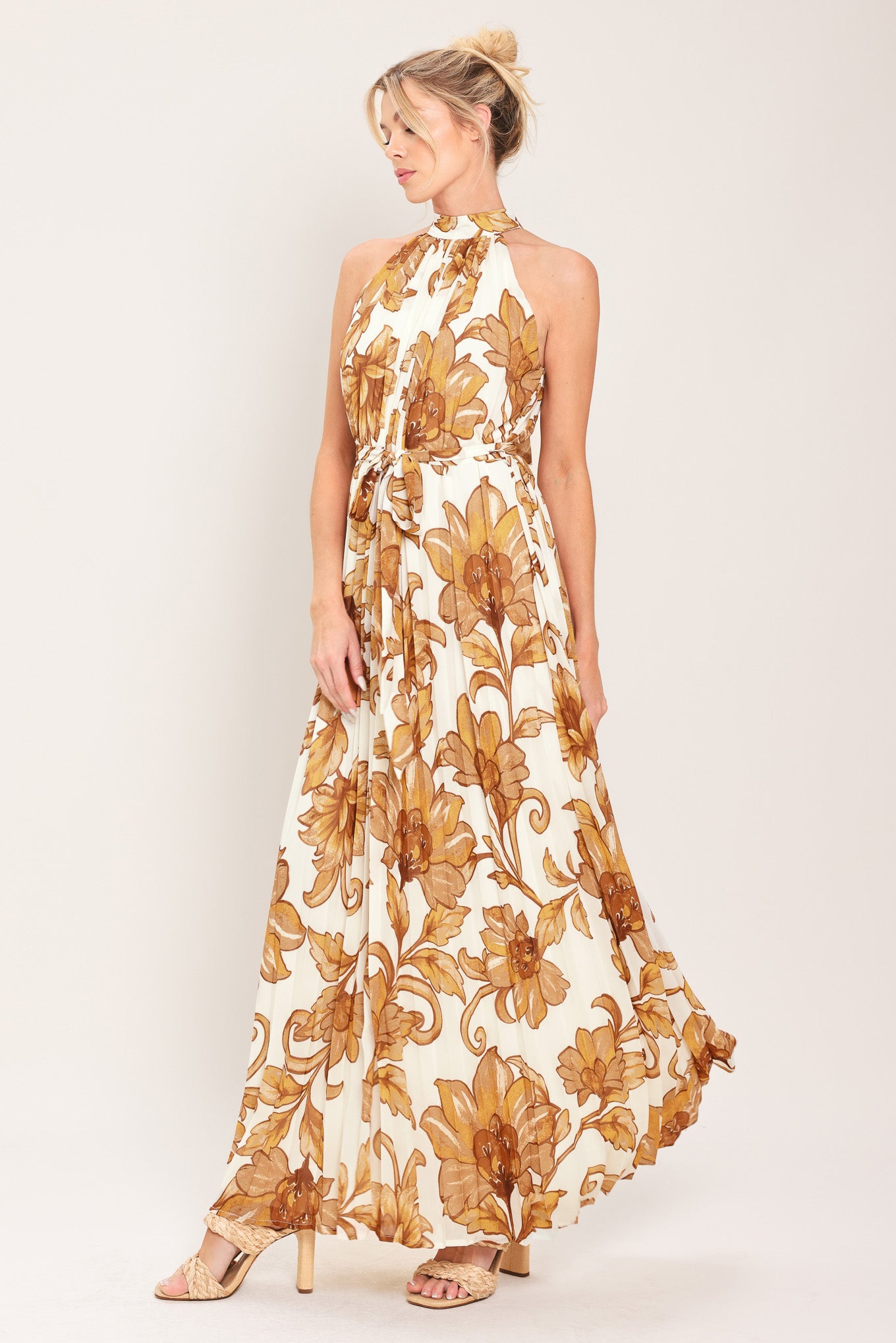 Woman wearing an ivory with brown floral print maxi dress with halter neckline with tie back, pleated body and self sash tie | Flying Tomato
