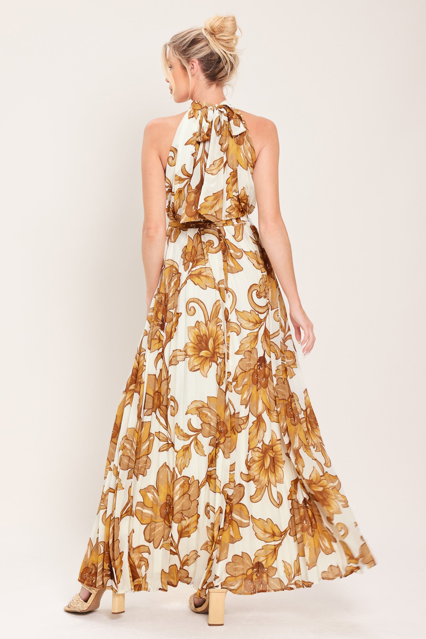 Woman wearing an ivory with brown floral print maxi dress with halter neckline with tie back, pleated body and self sash tie | Flying Tomato