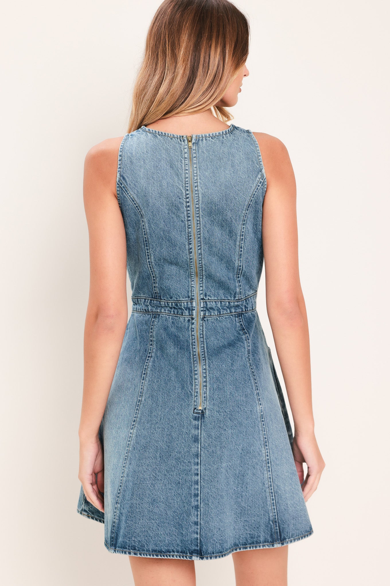 Woman wearing a mini denim dress featuring round neckline, sleeveless, front button down detail, side pockets, circle skirt and back zipper closure | Flying Tomato