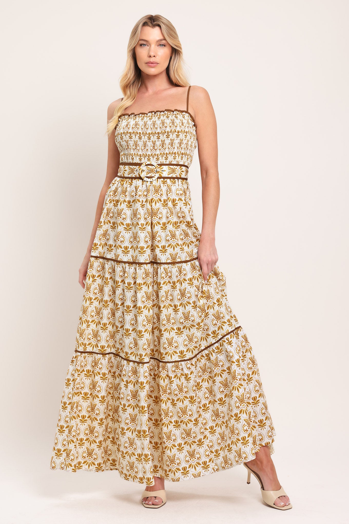 Woman wearing a green floral maxi dress featuring straight neckline with ruffle edge, straps, smocked bodice, self belt and tier skirt with piping inset | Flying Tomato