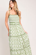 Woman wearing a green floral maxi dress featuring straight neckline with ruffle edge, straps, smocked bodice, self belt and tier skirt with piping inset | Flying Tomato