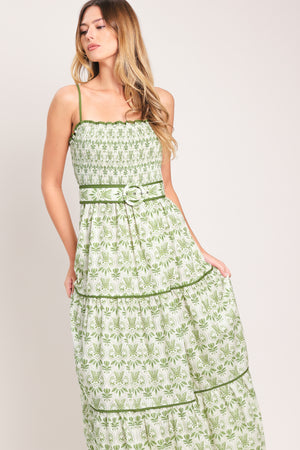 Woman wearing a green floral maxi dress featuring straight neckline with ruffle edge, straps, smocked bodice, self belt and tier skirt with piping inset | Flying Tomato