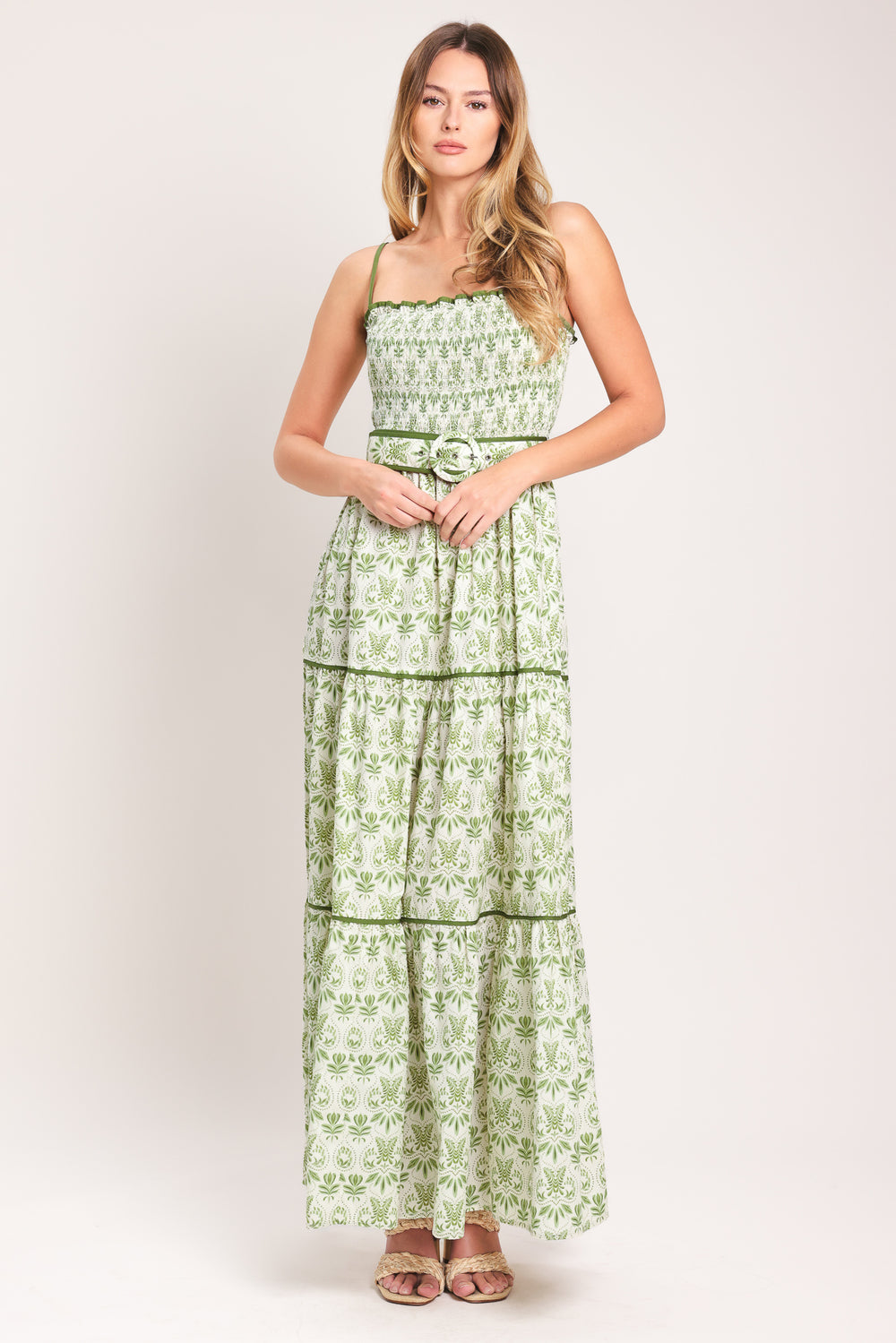 Woman wearing a green floral maxi dress featuring straight neckline with ruffle edge, straps, smocked bodice, self belt and tier skirt with piping inset | Flying Tomato