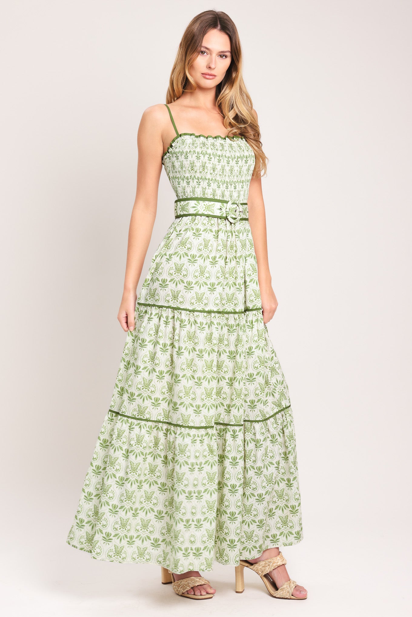 Woman wearing a green floral maxi dress featuring straight neckline with ruffle edge, straps, smocked bodice, self belt and tier skirt with piping inset | Flying Tomato