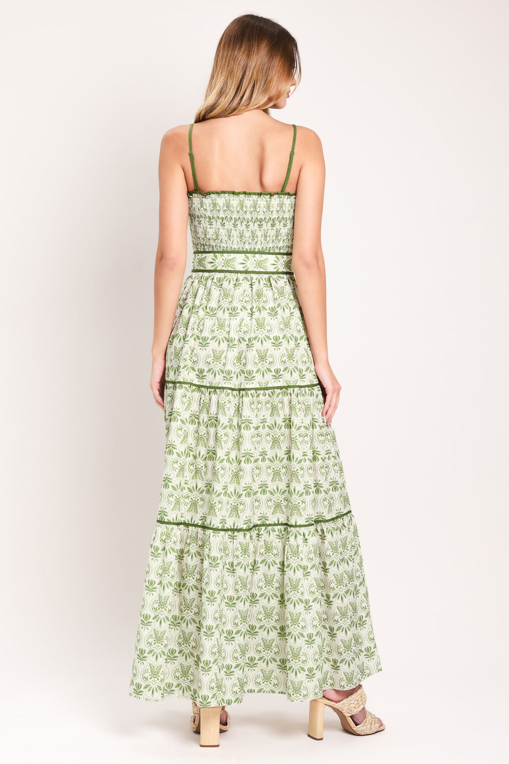 Woman wearing a green floral maxi dress featuring straight neckline with ruffle edge, straps, smocked bodice, self belt and tier skirt with piping inset | Flying Tomato