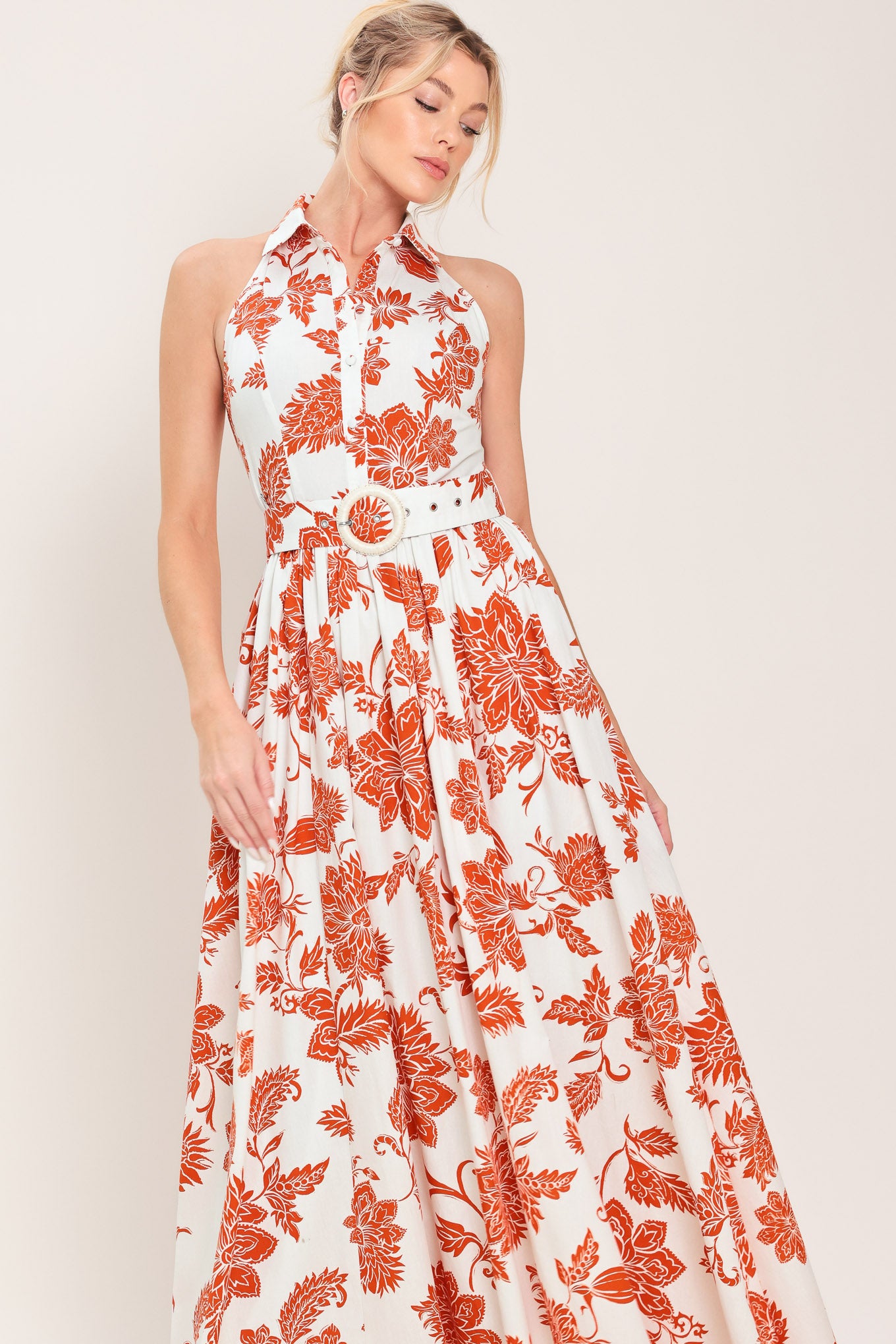 Woman wearing an ivory with rust-colored floral pattern maxi dress featuring halter neckline with collar, self belt, side pockets and full skirt | Flying Tomato