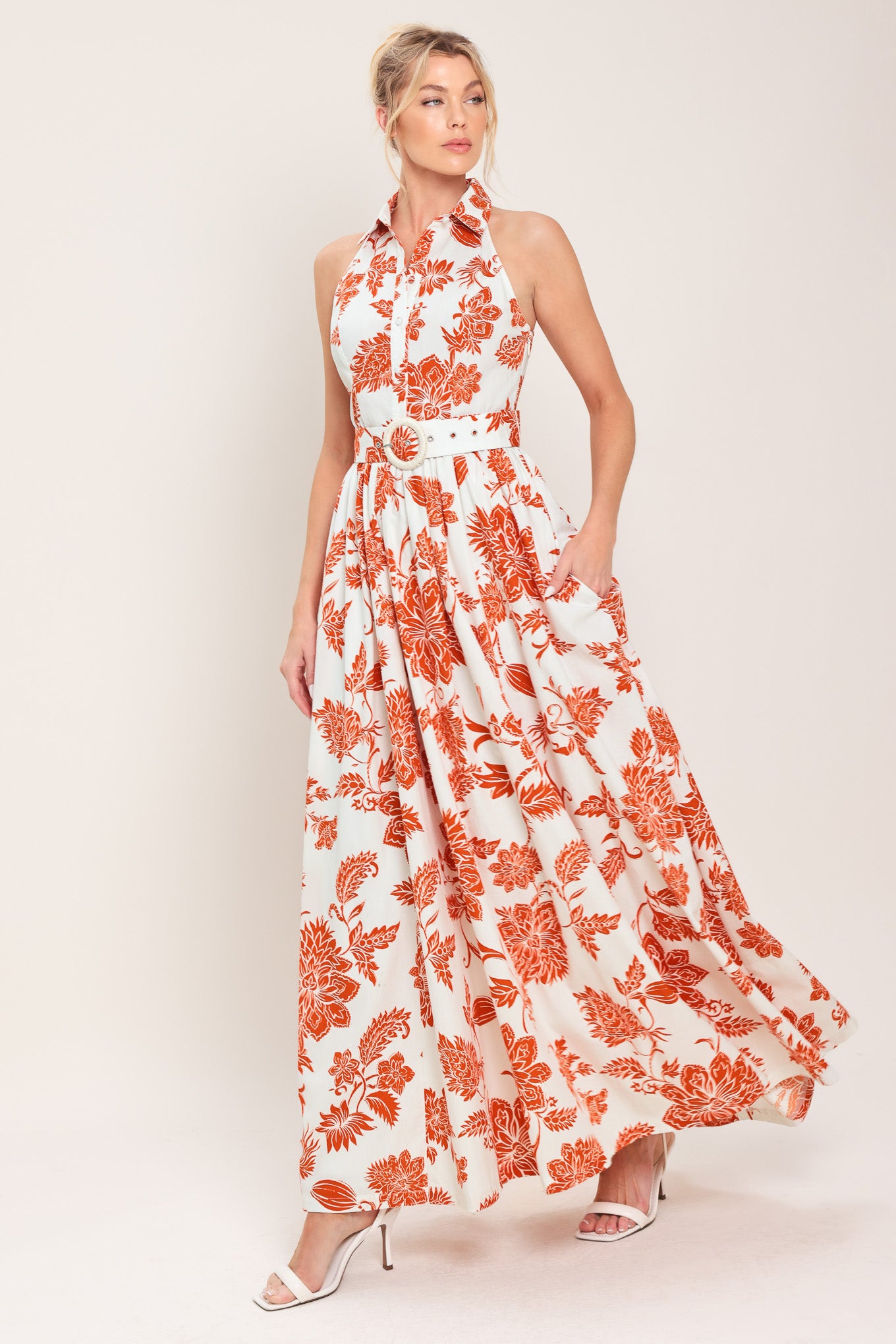 Woman wearing an ivory with rust-colored floral pattern maxi dress featuring halter neckline with collar, self belt, side pockets and full skirt | Flying Tomato