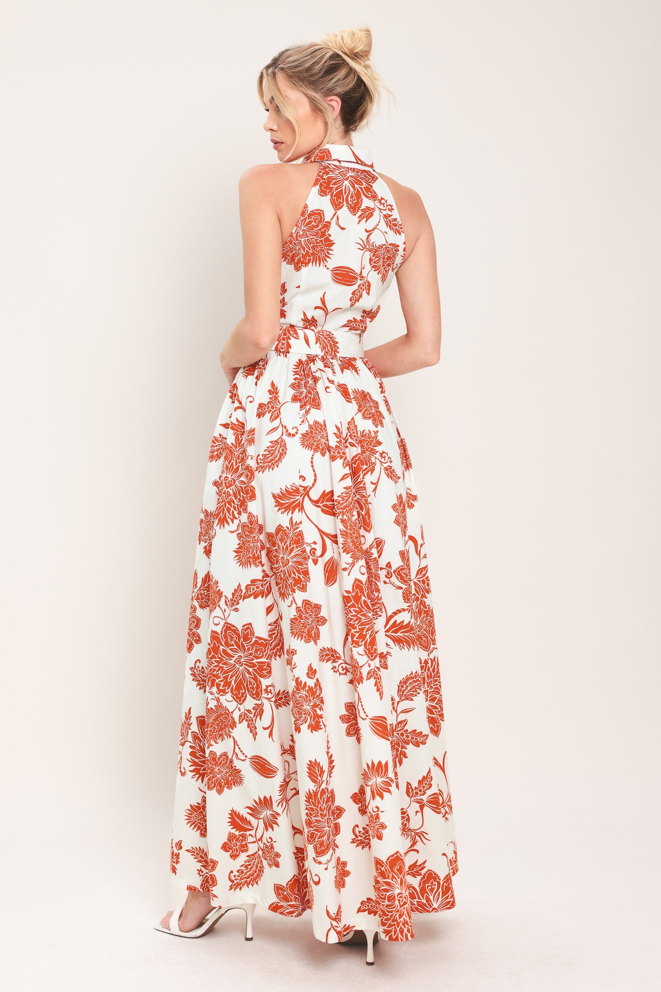 Woman wearing an ivory with rust-colored floral pattern maxi dress featuring halter neckline with collar, self belt, side pockets and full skirt | Flying Tomato