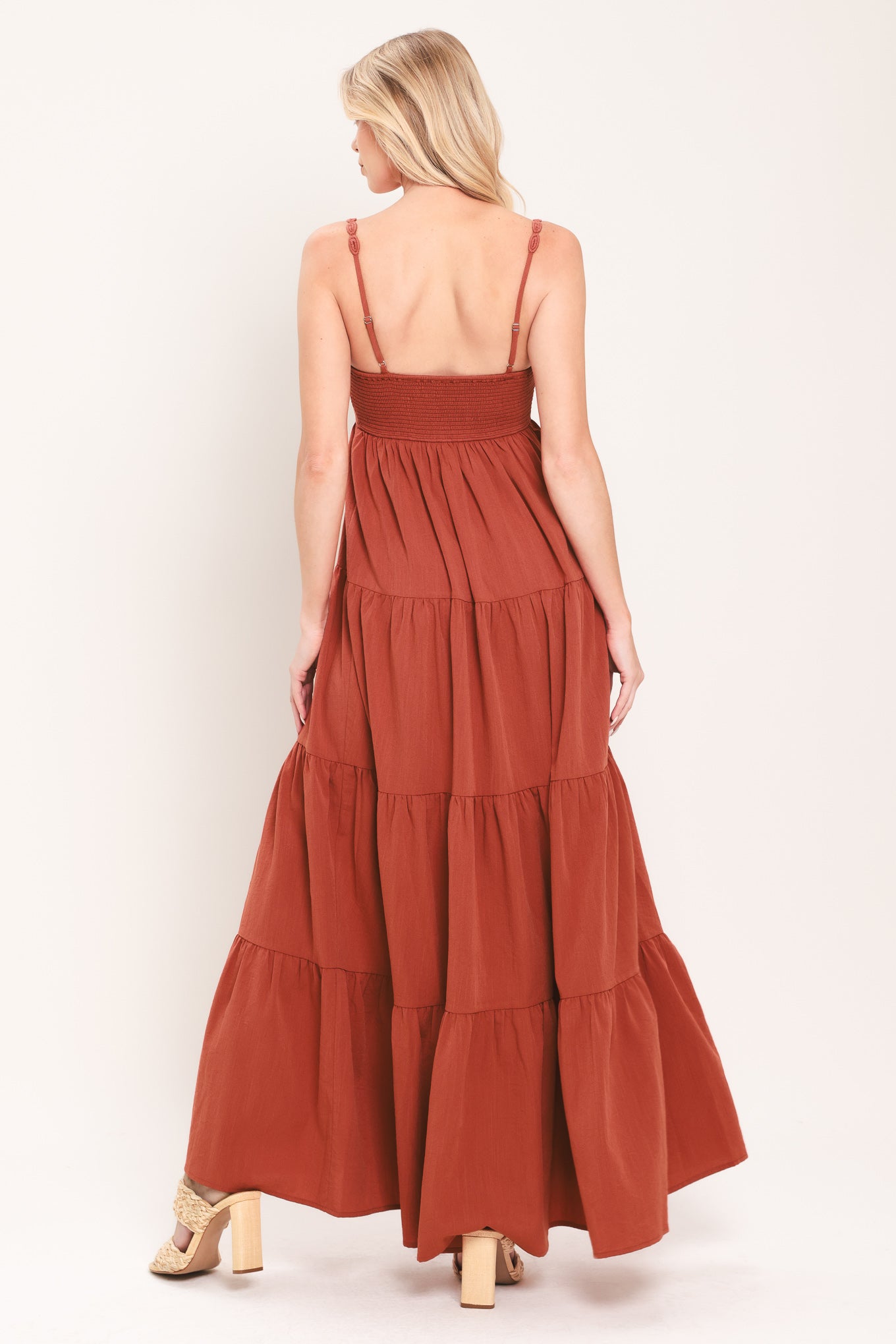 Woman wearing a rust-colored tiered maxi dress featuring cami top with O ring and cut out, lace straps, and smocked back bodice | Flying Tomato