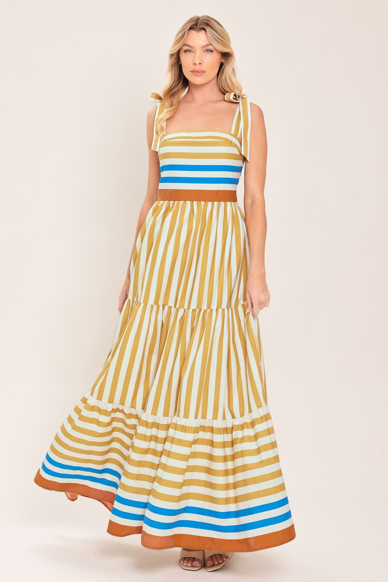 A woman wearing a sleeveless tiered maxi dress with horizontal stripes in mustard yellow, white, blue, and brown | Flying Tomato