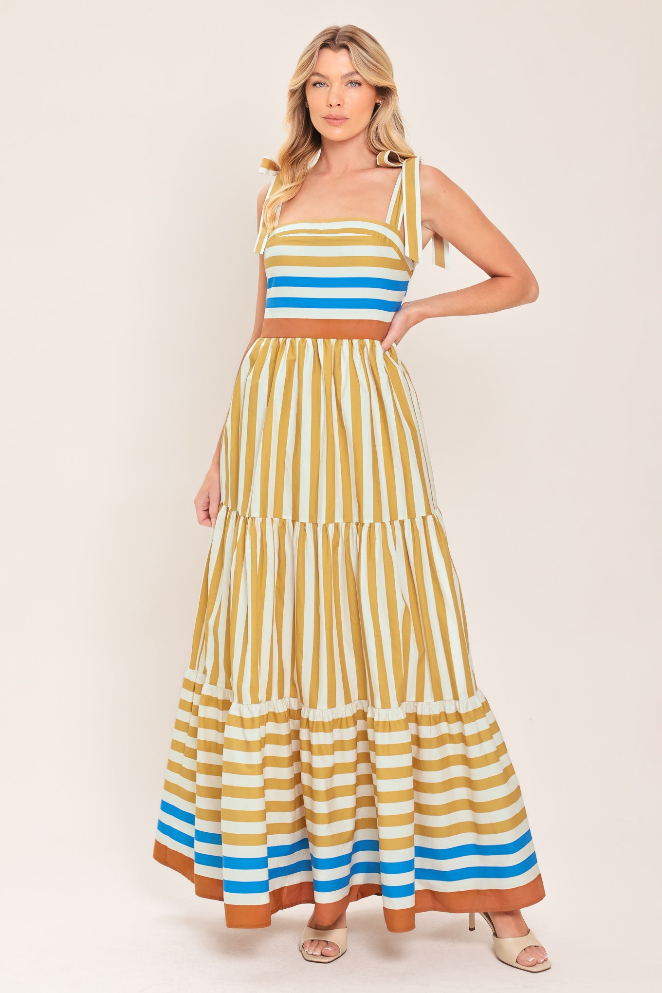 A woman wearing a sleeveless tiered maxi dress with horizontal stripes in mustard yellow, white, blue, and brown | Flying Tomato