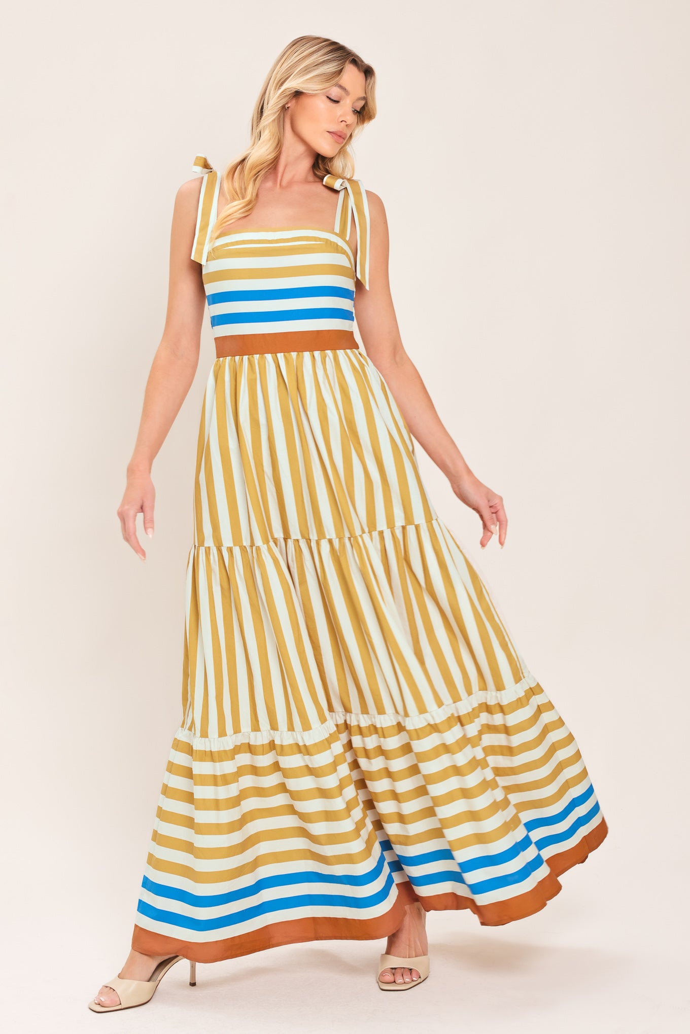 A woman wearing a sleeveless tiered maxi dress with horizontal stripes in mustard yellow, white, blue, and brown | Flying Tomato