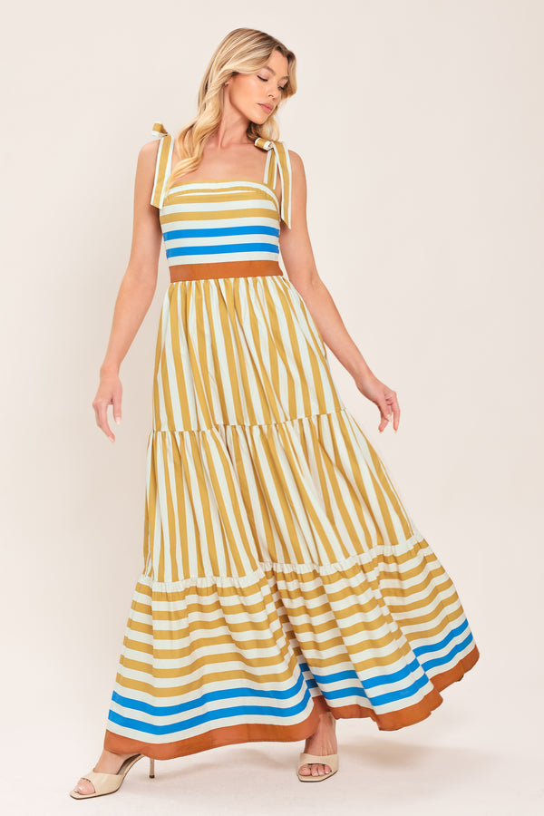 A woman wearing a sleeveless tiered maxi dress with horizontal stripes in mustard yellow, white, blue, and brown | Flying Tomato