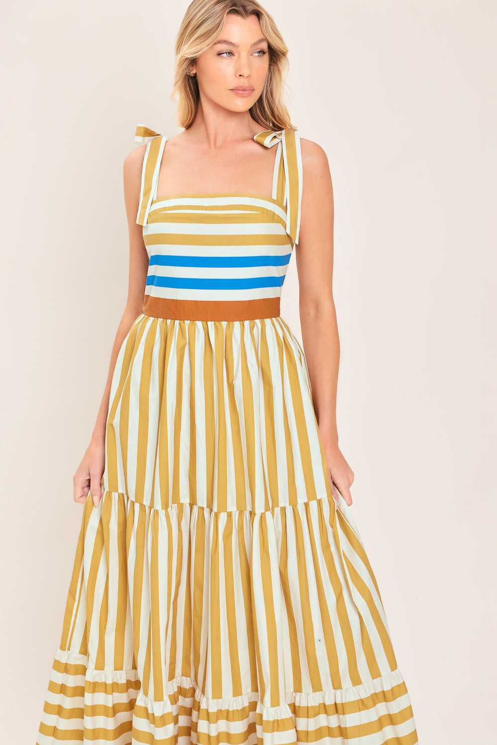 A woman wearing a sleeveless tiered maxi dress with horizontal stripes in mustard yellow, white, blue, and brown | Flying Tomato