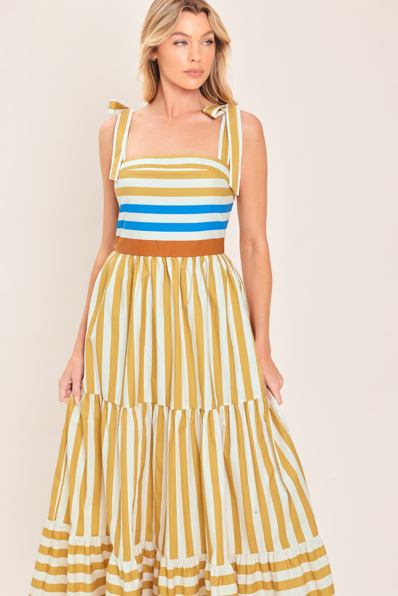 A woman wearing a sleeveless tiered maxi dress with horizontal stripes in mustard yellow, white, blue, and brown | Flying Tomato