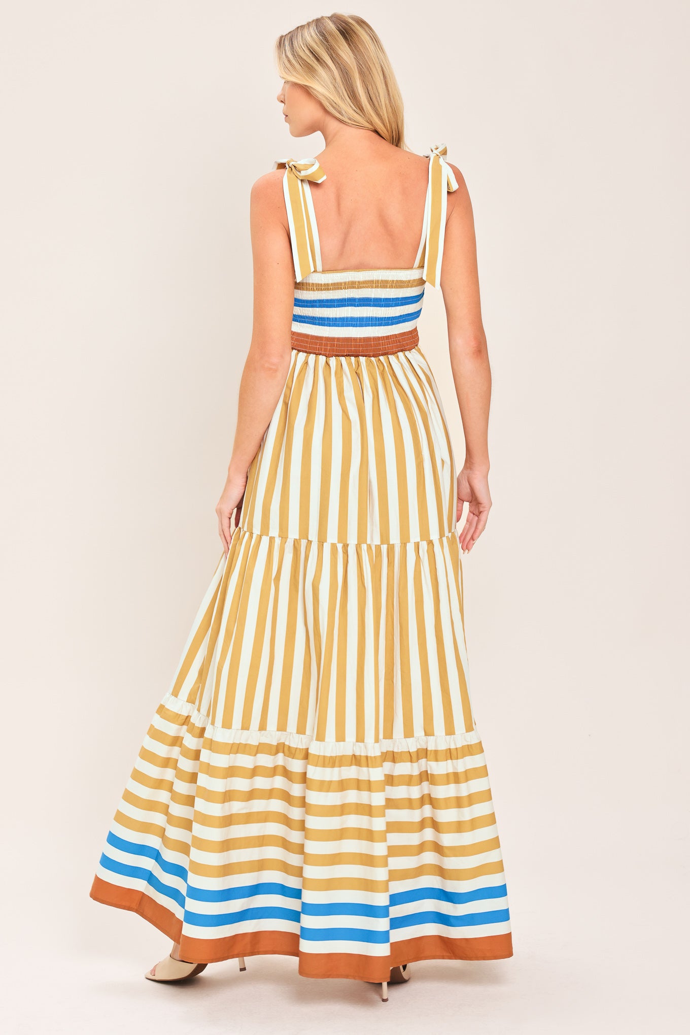 A woman wearing a sleeveless tiered maxi dress with horizontal stripes in mustard yellow, white, blue, and brown | Flying Tomato