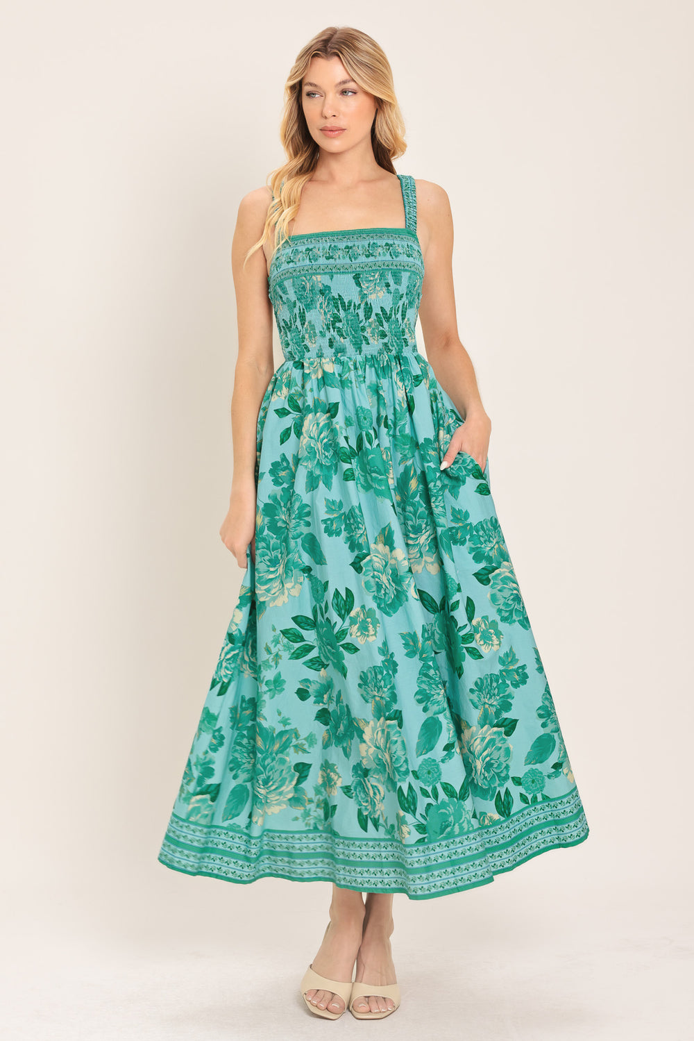 Woman wearing a teal floral midi dress featuring straight neckline with smocked bodice, full skirt and bare back with strap detail | Flying Tomato