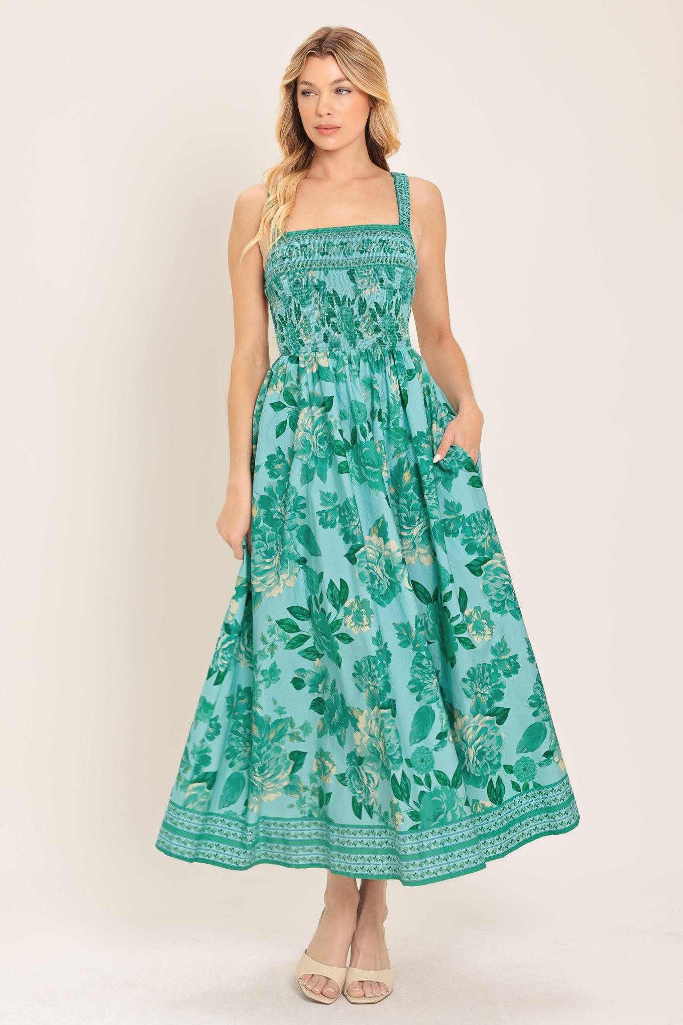 Woman wearing a teal floral midi dress featuring straight neckline with smocked bodice, full skirt and bare back with strap detail | Flying Tomato