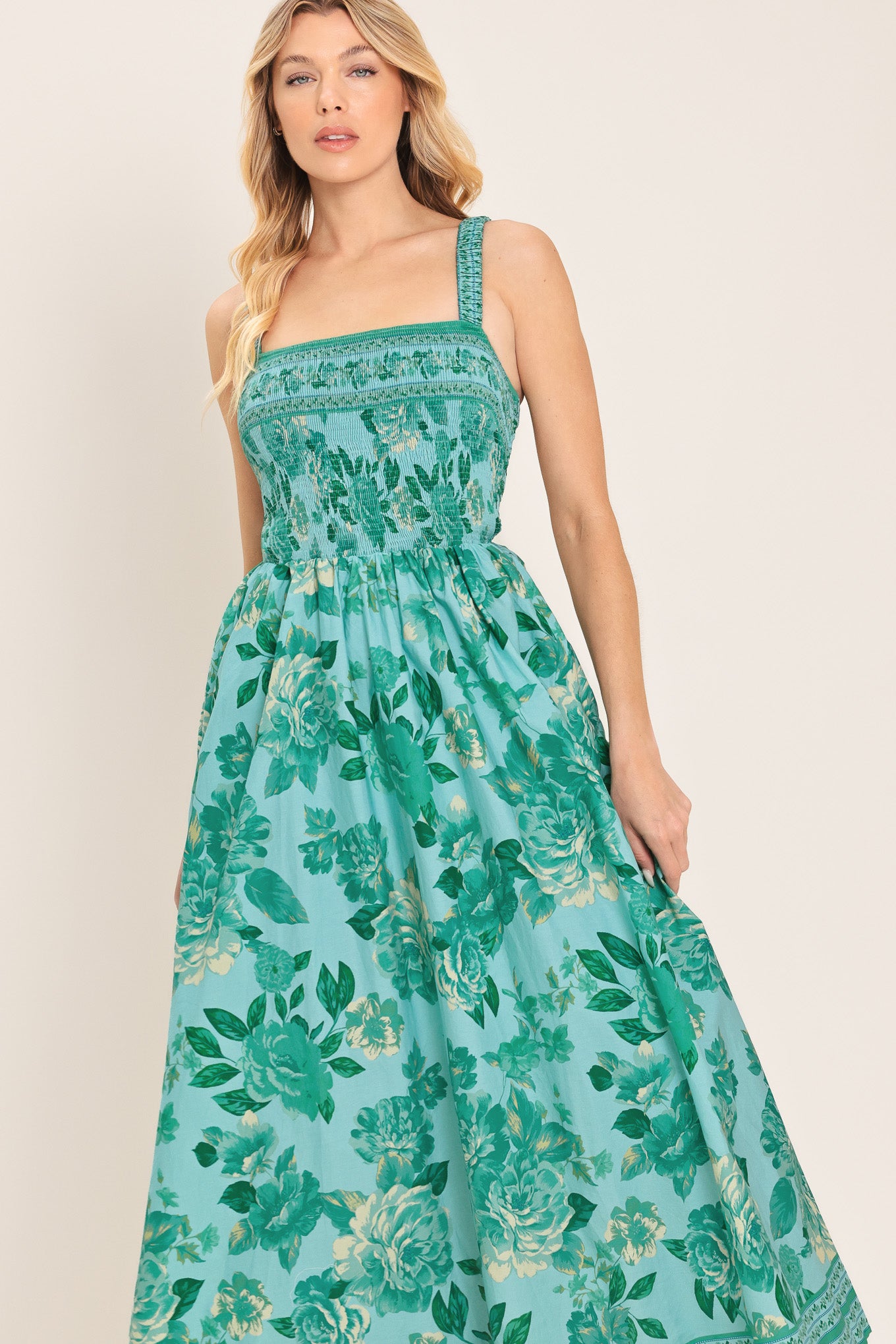 Woman wearing a teal floral midi dress featuring straight neckline with smocked bodice, full skirt and bare back with strap detail | Flying Tomato
