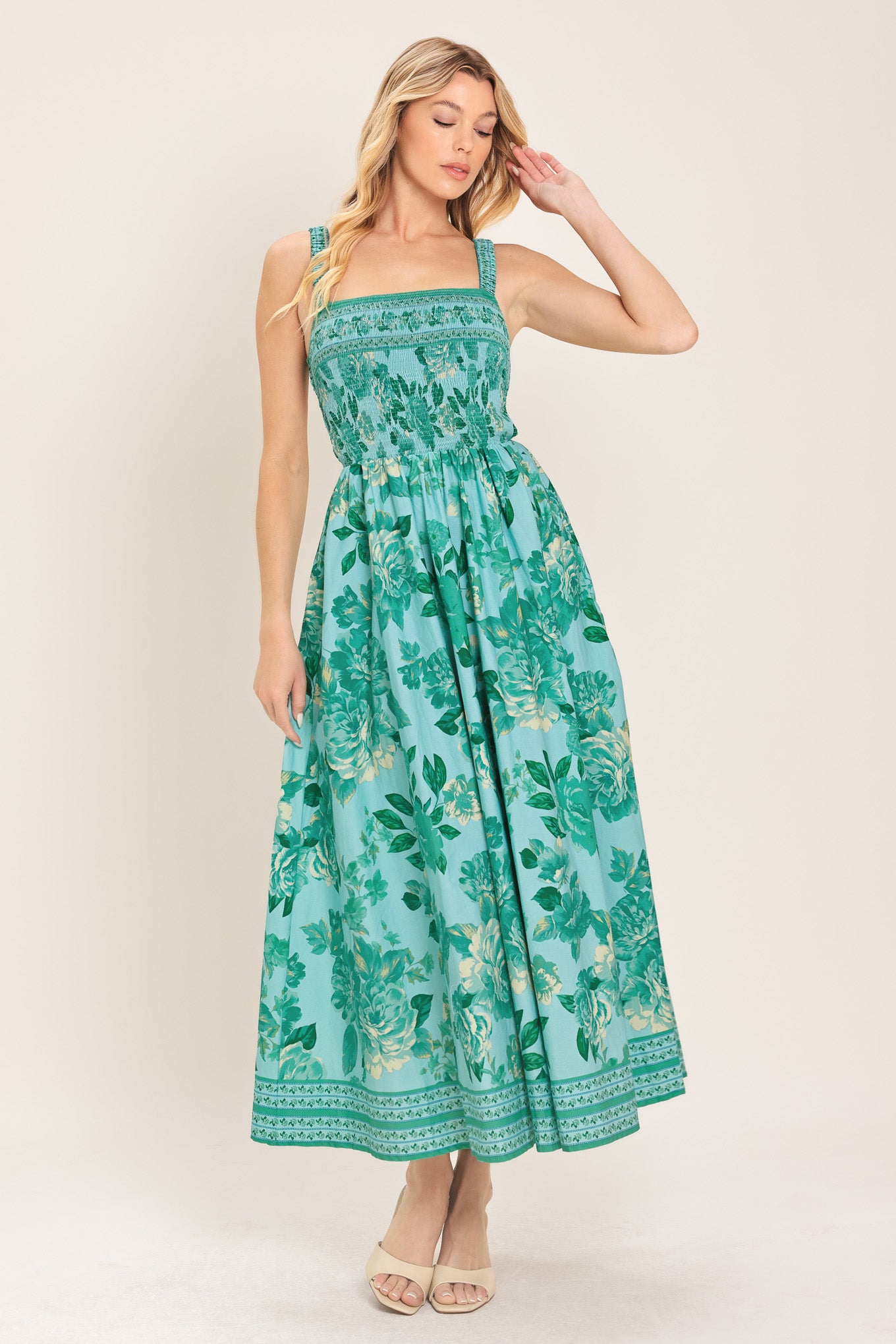 Woman wearing a teal floral midi dress featuring straight neckline with smocked bodice, full skirt and bare back with strap detail | Flying Tomato