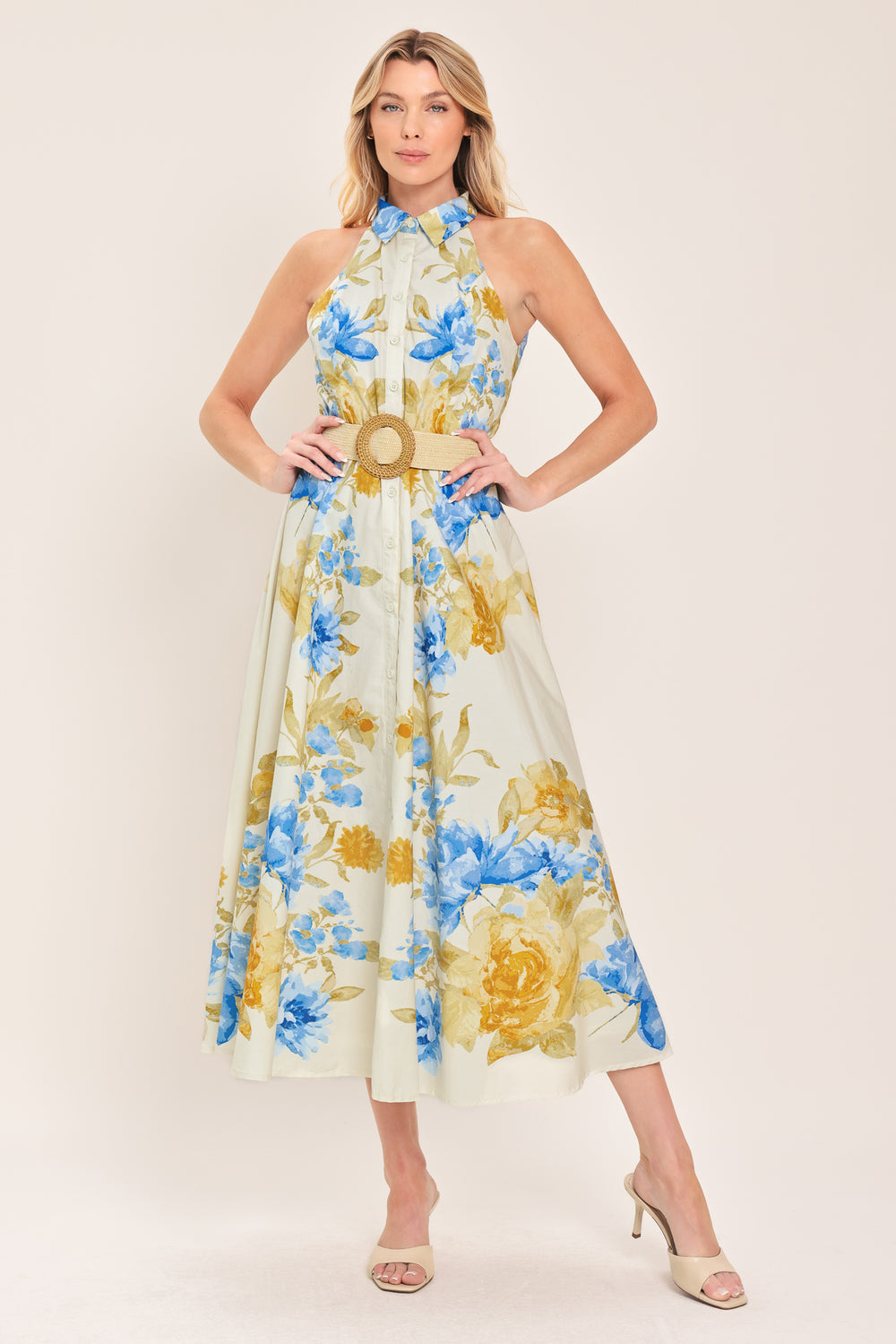 Woman wearing a sleeveless floral midi dress with blue and yellow flowers featuring a collar, front button closure and contrasting belt | Flying Tomato
