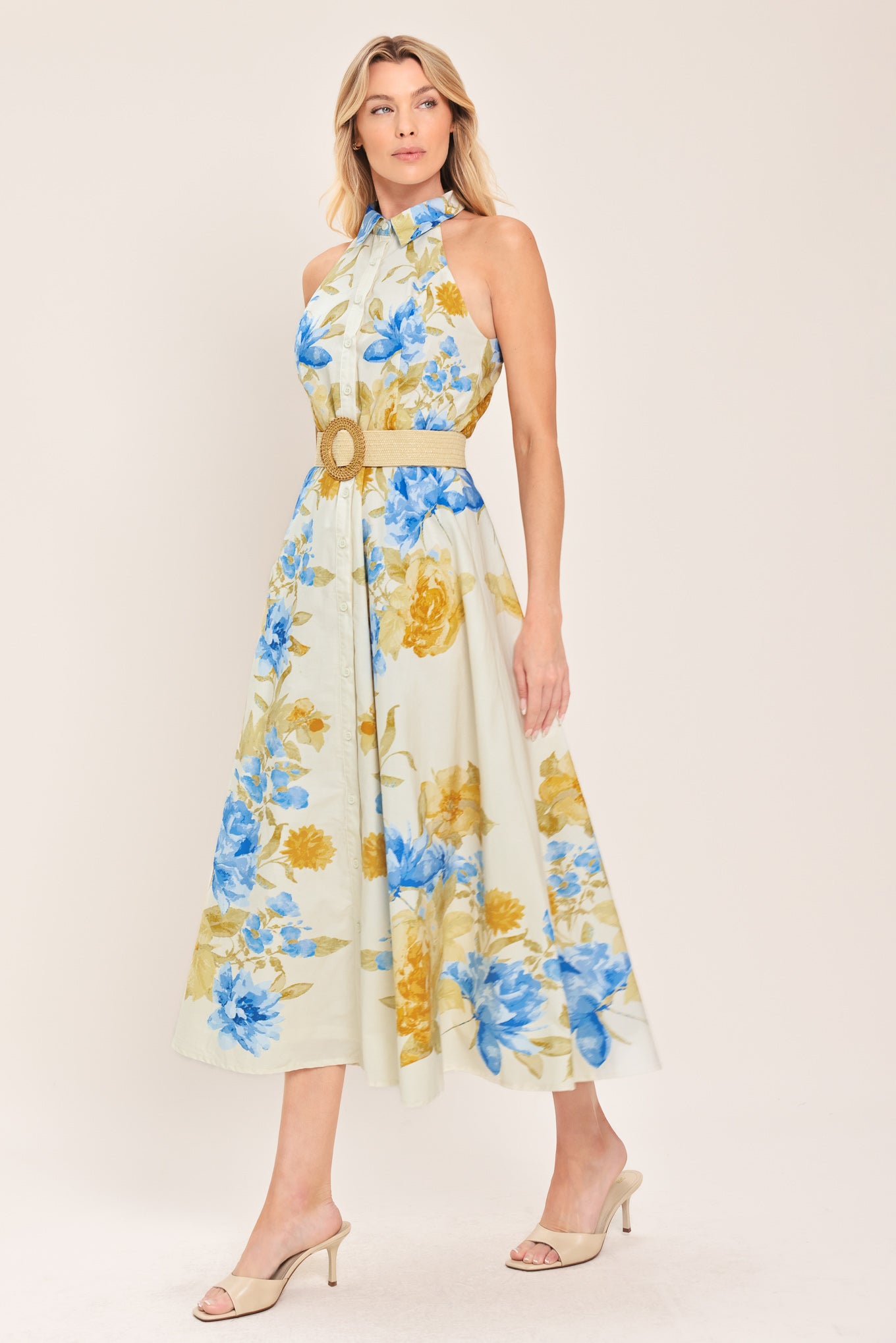 Woman wearing a sleeveless floral midi dress with blue and yellow flowers featuring a collar, front button closure and contrasting belt | Flying Tomato