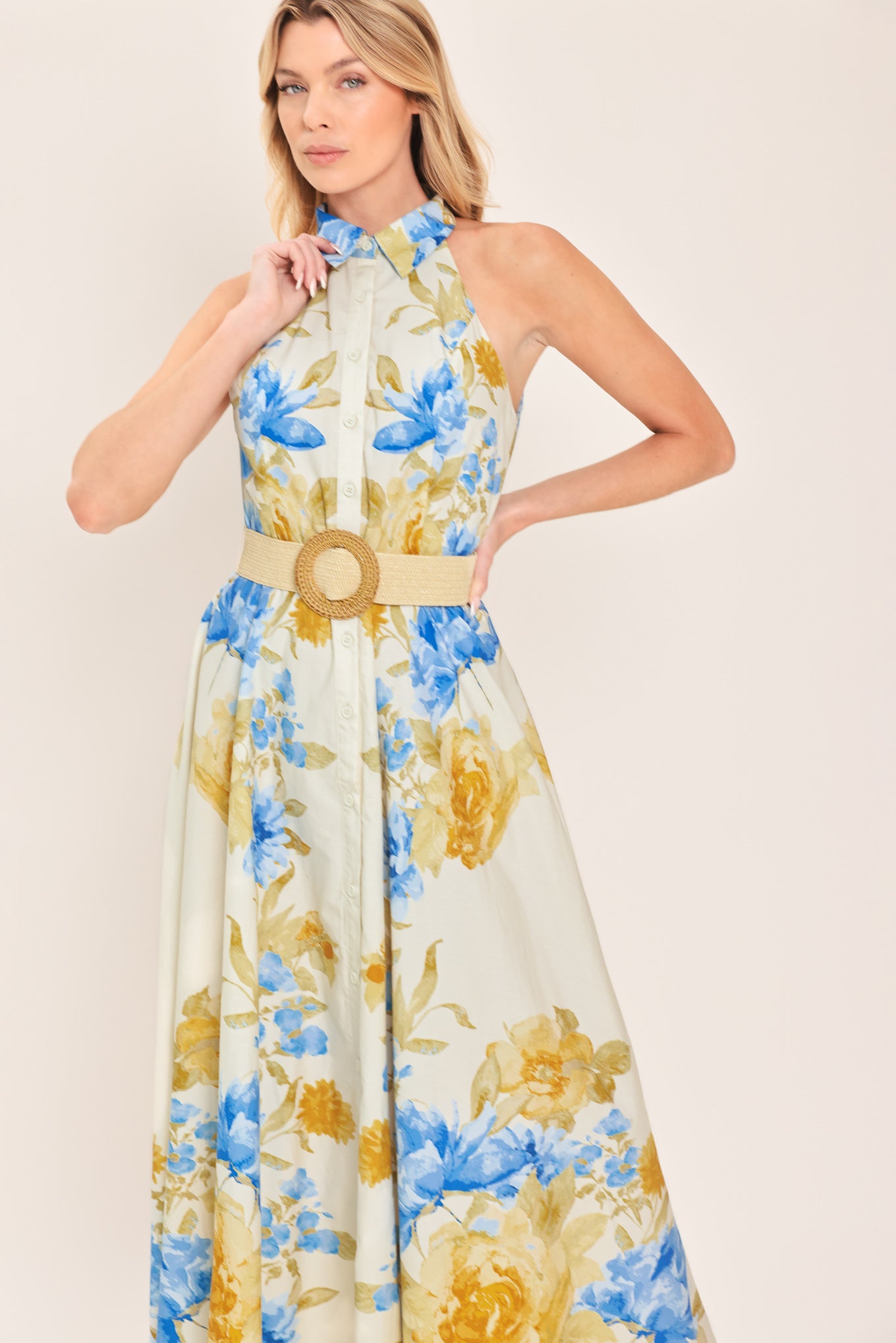 Woman wearing a sleeveless floral midi dress with blue and yellow flowers featuring a collar, front button closure and contrasting belt | Flying Tomato