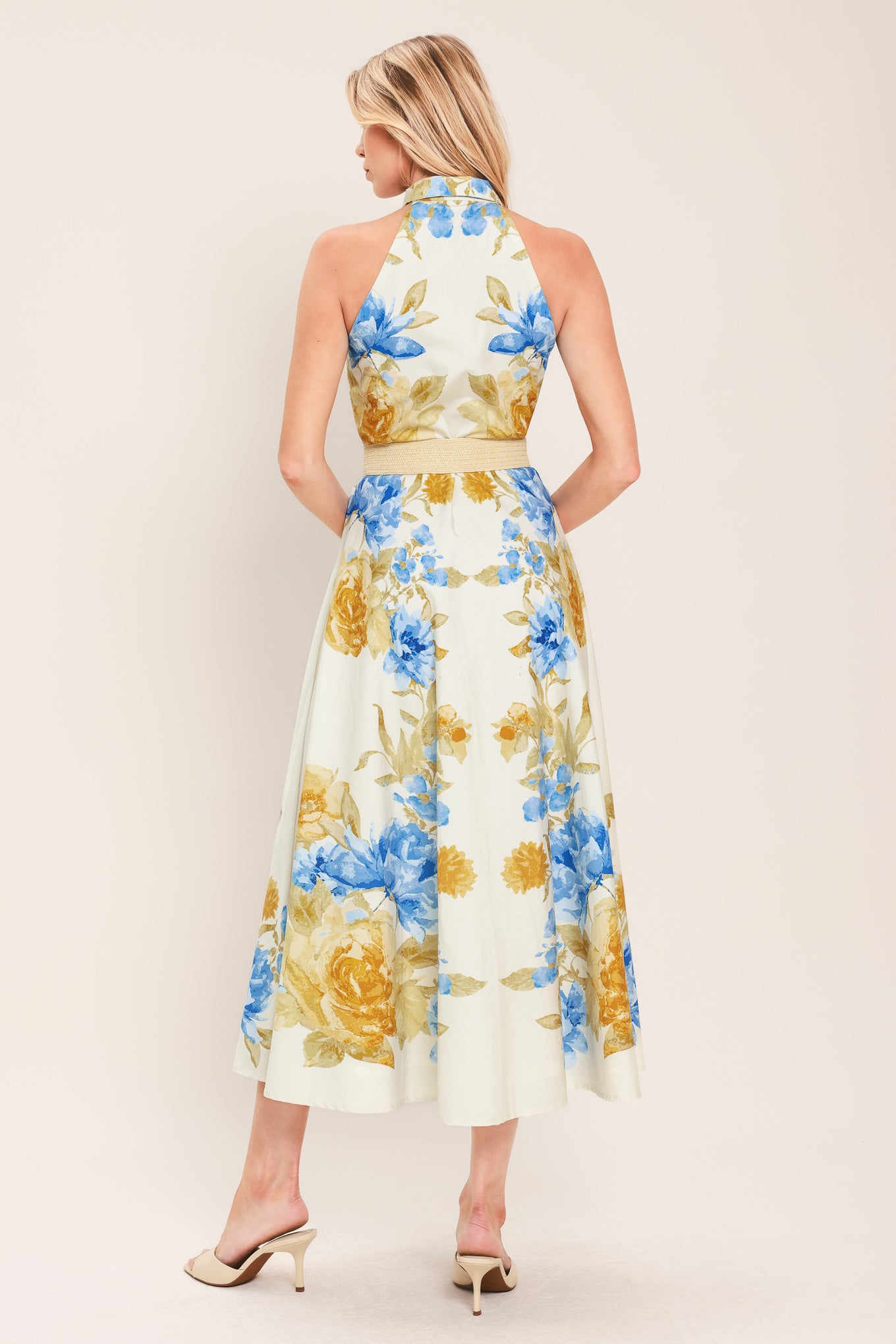 Woman wearing a sleeveless floral midi dress with blue and yellow flowers featuring a collar, front button closure and contrasting belt | Flying Tomato