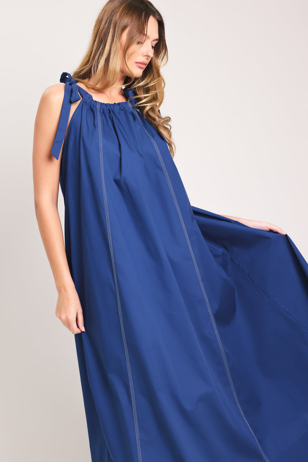 Woman wearing a blue midi dress with bow straps and pockets | Flying Tomato