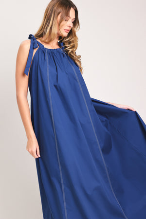 Woman wearing a blue midi dress with bow straps and pockets | Flying Tomato