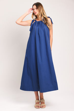 Woman wearing a blue midi dress with bow straps and pockets | Flying Tomato