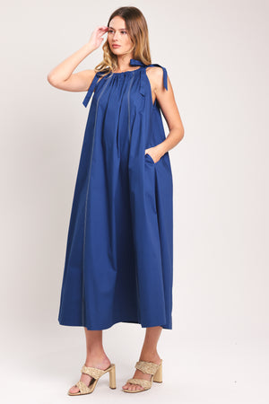 Woman wearing a blue midi dress with bow straps and pockets | Flying Tomato