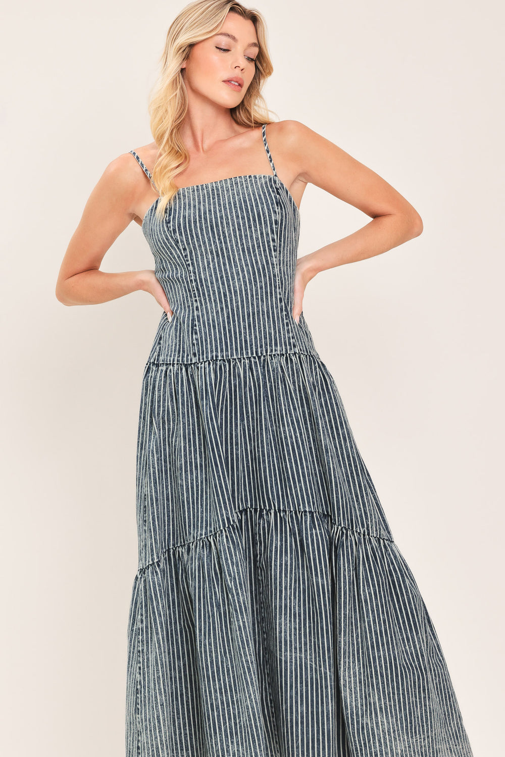 Woman wearing a blue striped washed denim midi dress featuring straight neckline, straps, drop waistline, single tier and back zipper closure | Flying Tomato