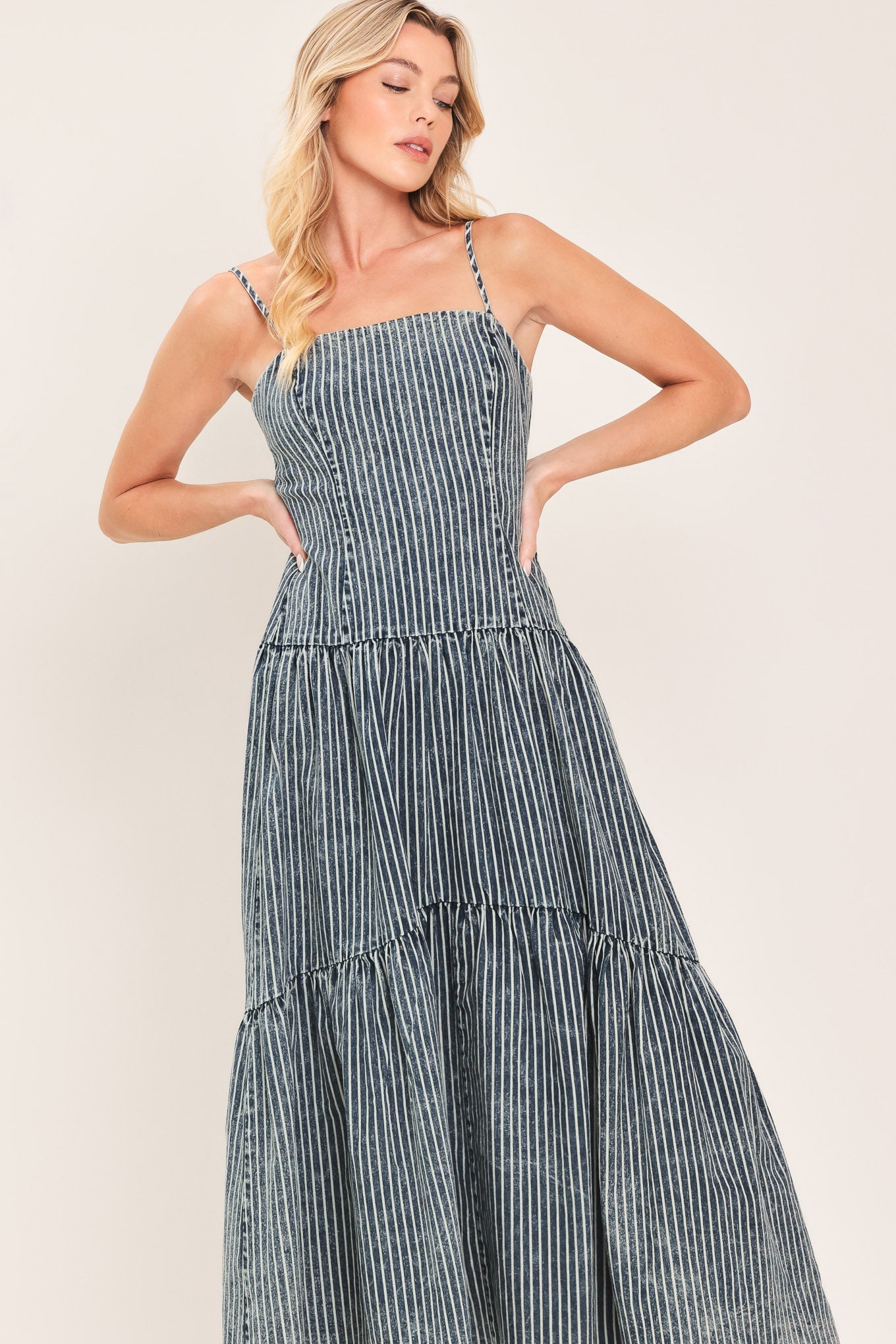 Woman wearing a blue striped washed denim midi dress featuring straight neckline, straps, drop waistline, single tier and back zipper closure | Flying Tomato