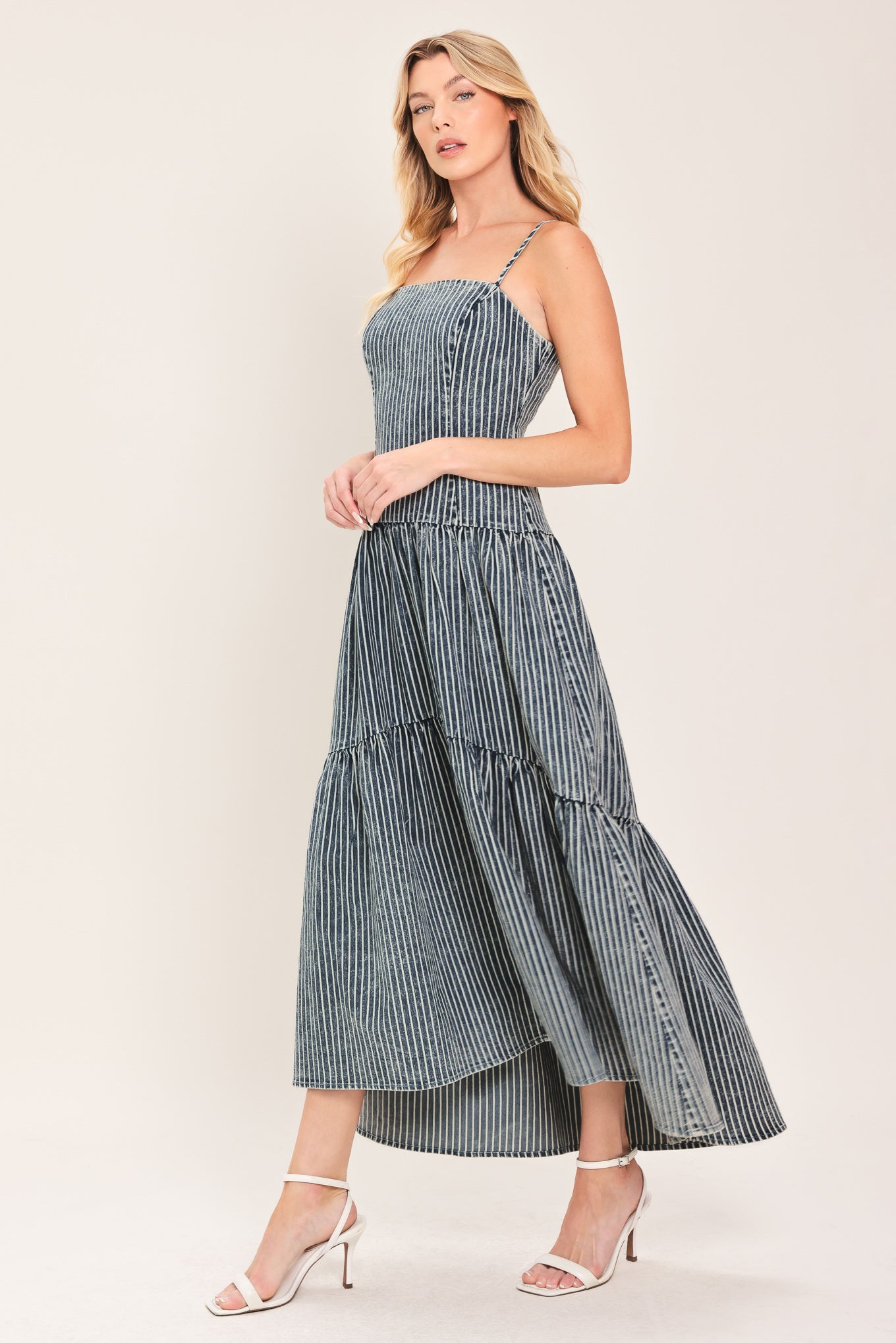 Woman wearing a blue striped washed denim midi dress featuring straight neckline, straps, drop waistline, single tier and back zipper closure | Flying Tomato