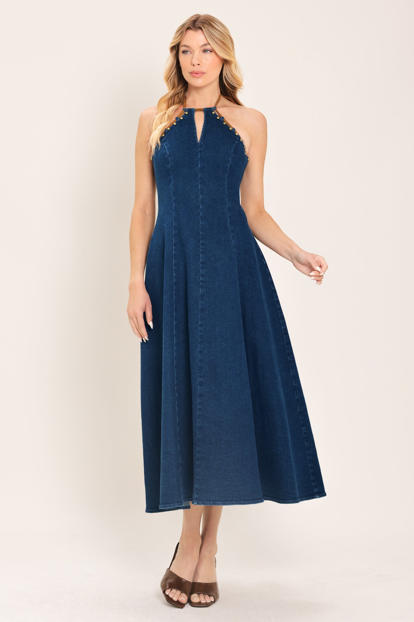 Woman wearing a blue denim midi dress featuring halter neckline with contrasting tie, stud detail, circle skirt and back zipper closure | Flying Tomato