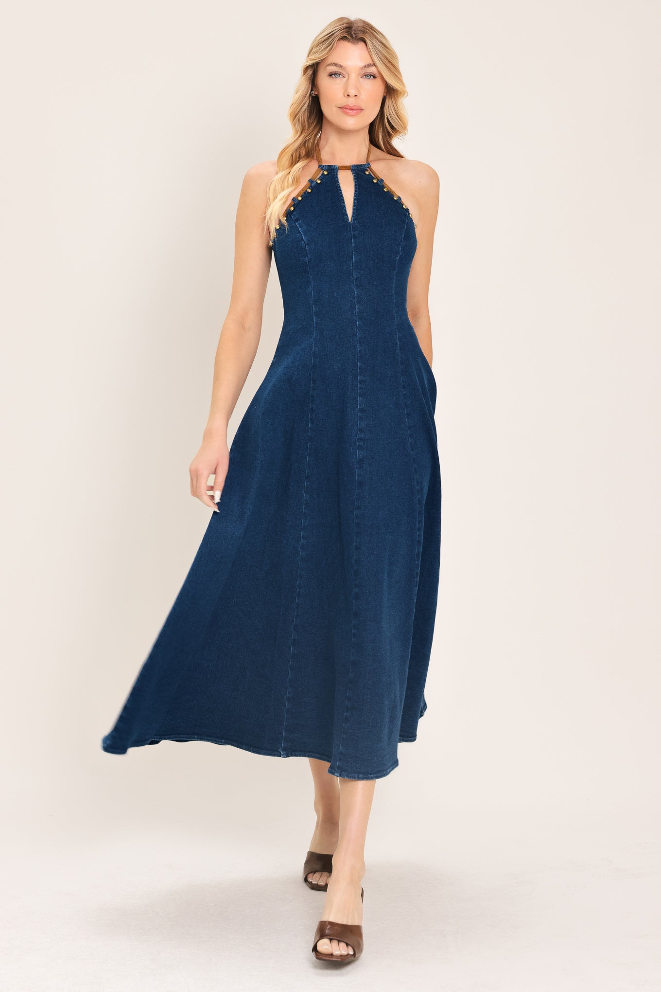 Woman wearing a blue denim midi dress featuring halter neckline with contrasting tie, stud detail, circle skirt and back zipper closure | Flying Tomato