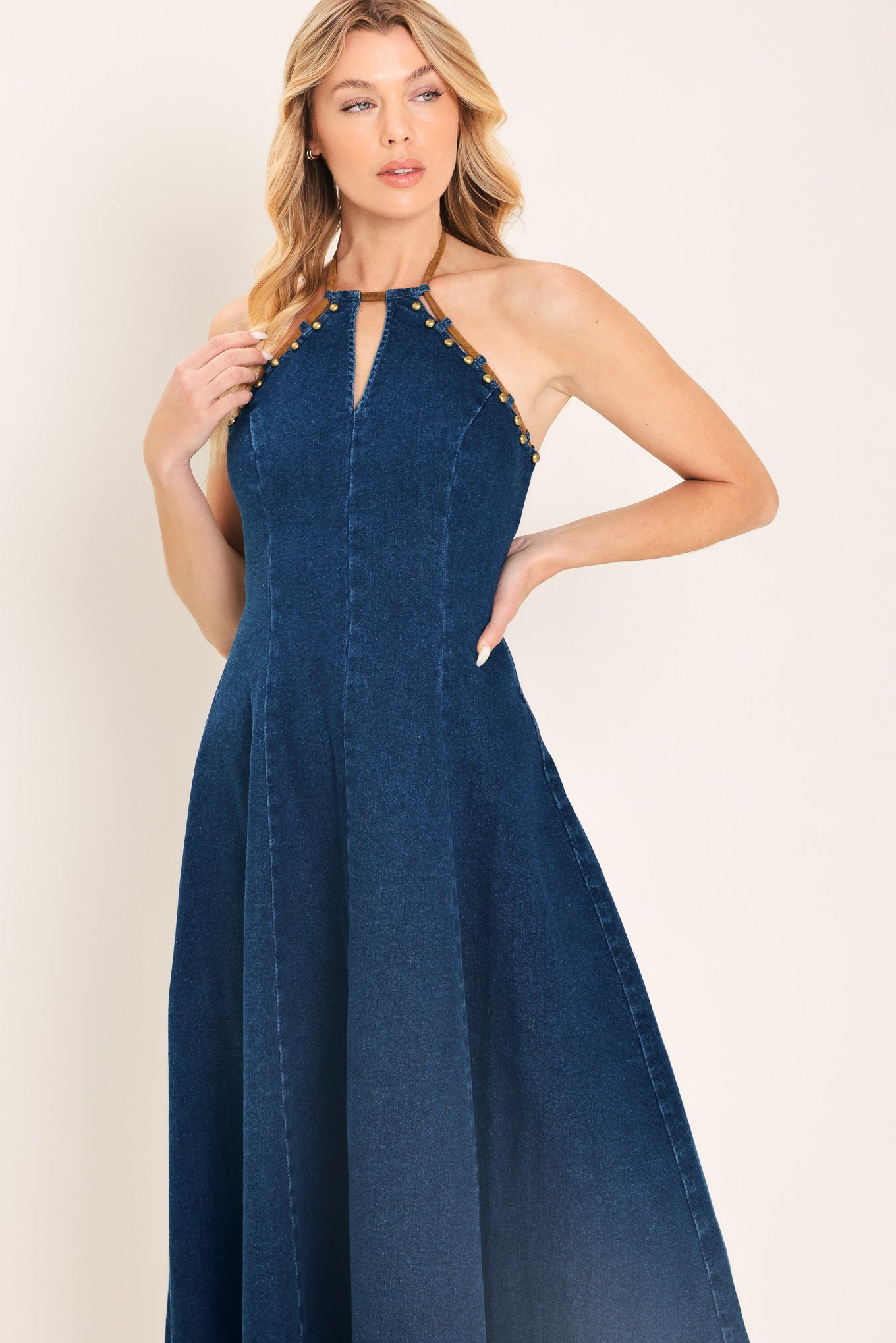 Woman wearing a blue denim midi dress featuring halter neckline with contrasting tie, stud detail, circle skirt and back zipper closure | Flying Tomato