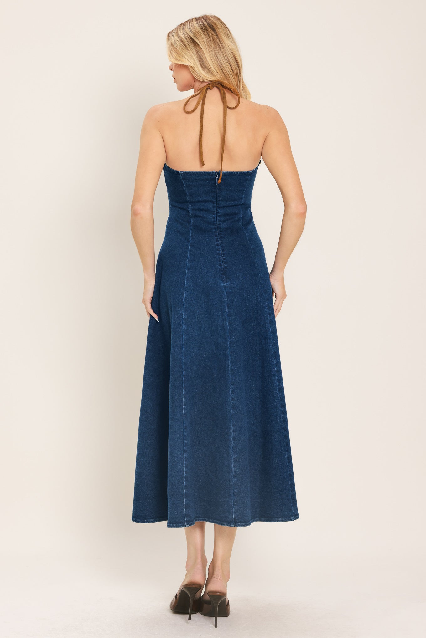 Woman wearing a blue denim midi dress featuring halter neckline with contrasting tie, stud detail, circle skirt and back zipper closure | Flying Tomato
