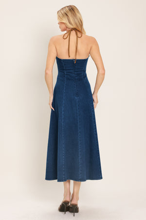 Woman wearing a blue denim midi dress featuring halter neckline with contrasting tie, stud detail, circle skirt and back zipper closure | Flying Tomato