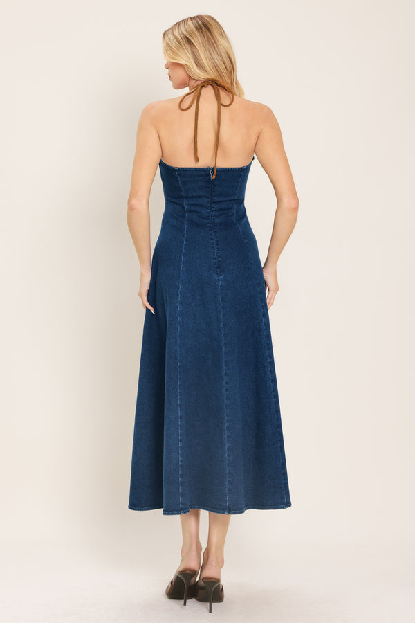 Woman wearing a blue denim midi dress featuring halter neckline with contrasting tie, stud detail, circle skirt and back zipper closure | Flying Tomato