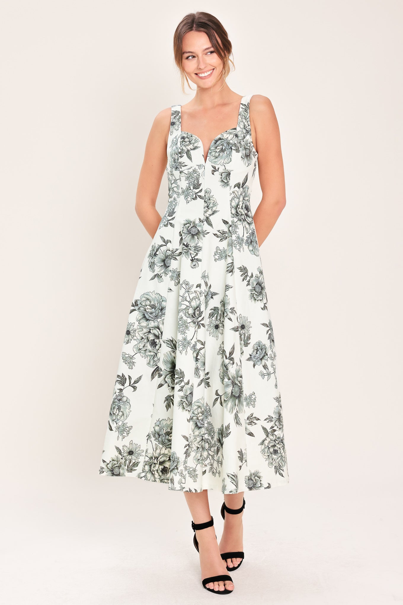 Woman wearing a black and white floral midi dress featuring sweetheart neckline, straps, circle skirt and back zipper closure | Flying Tomato