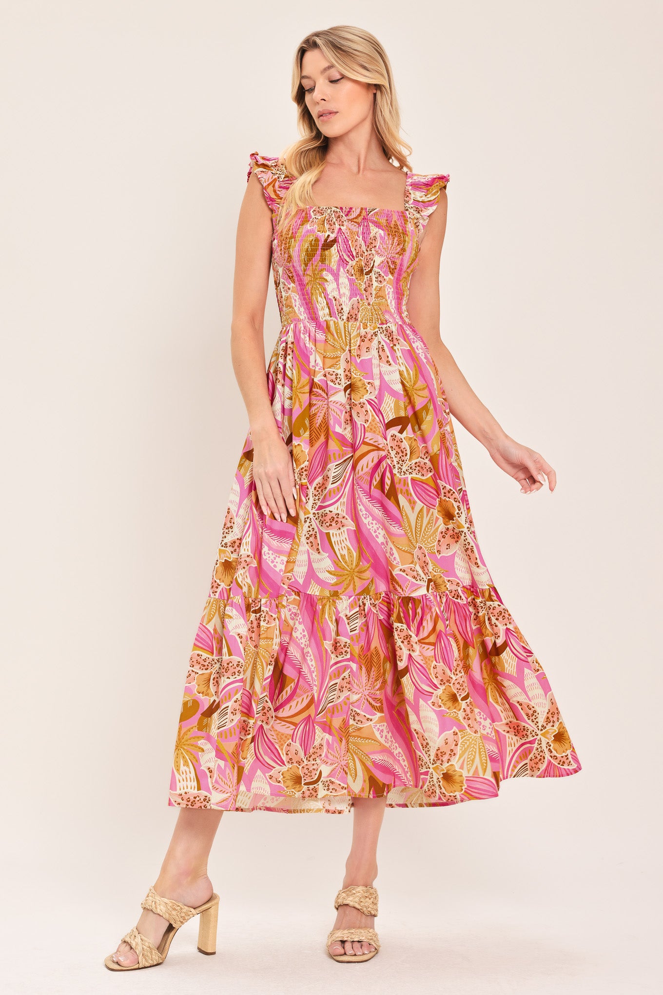 Woman wearing a pink tropical floral midi dress featuring square neckline, ruffle sleeve, smocked bodice and tier skirt | Flying Tomato